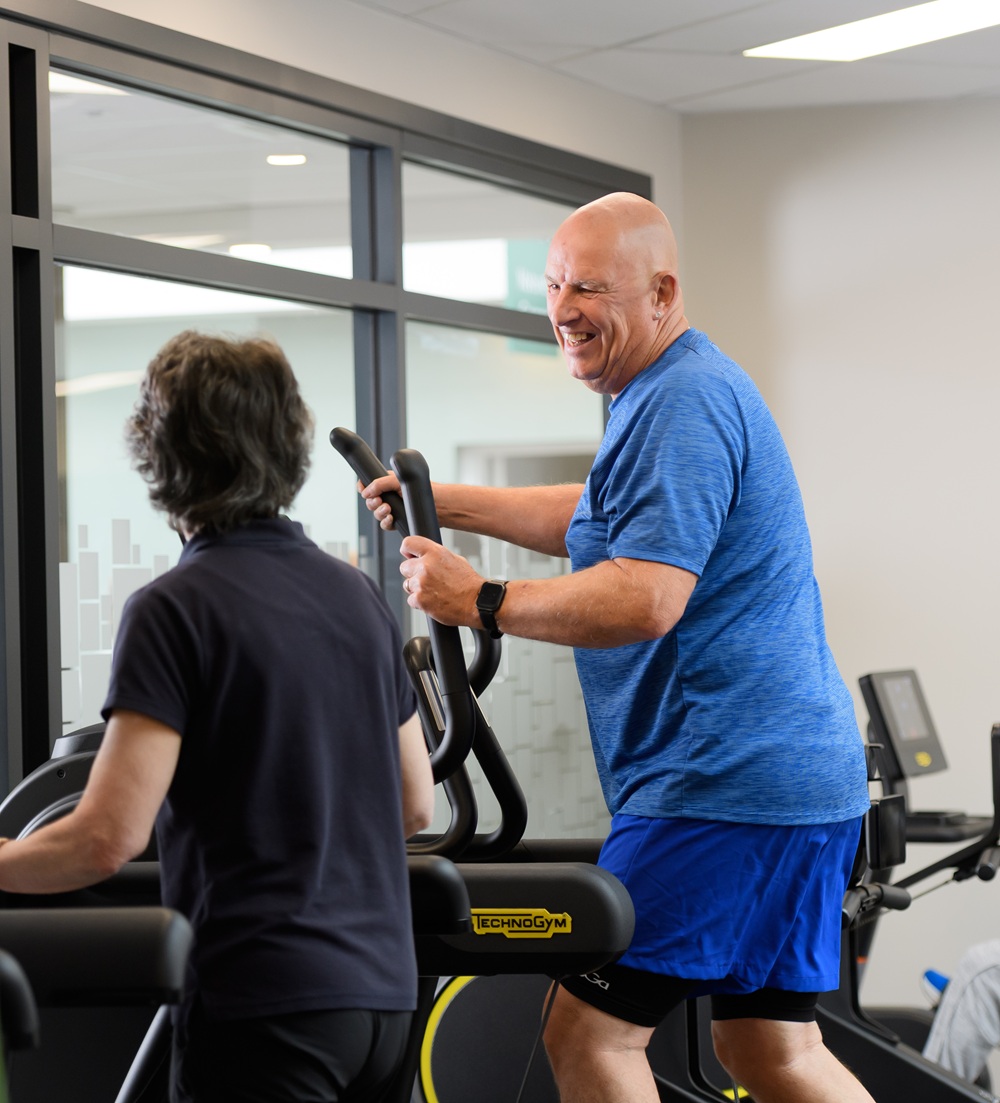 Man in blue t shirt on the cross trainer talking to a lady in a black t shirt on the treadmill
